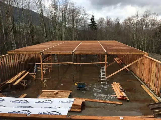 Wood-framed walls and floor of a building under construction with trees behind