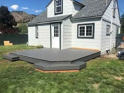 Low gray backyard deck with wide steps beside a white house and lawn