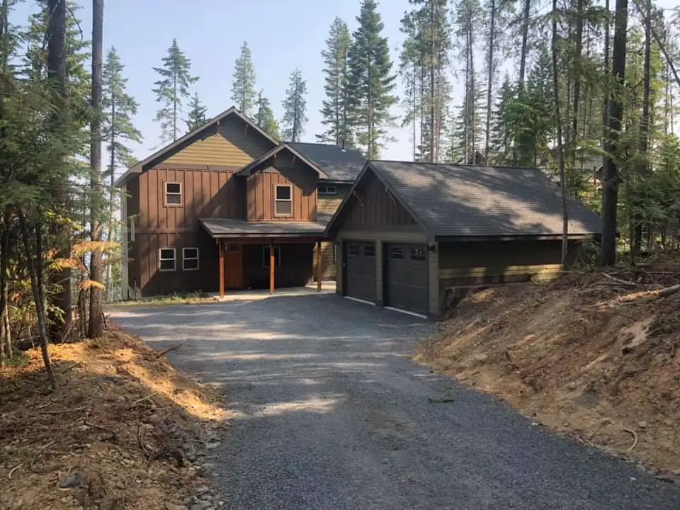 Two-story home with brown board-and-batten siding and an attached two-car garage among the pines, from the project photos of a remodeling contractor in Wenatchee, WA
