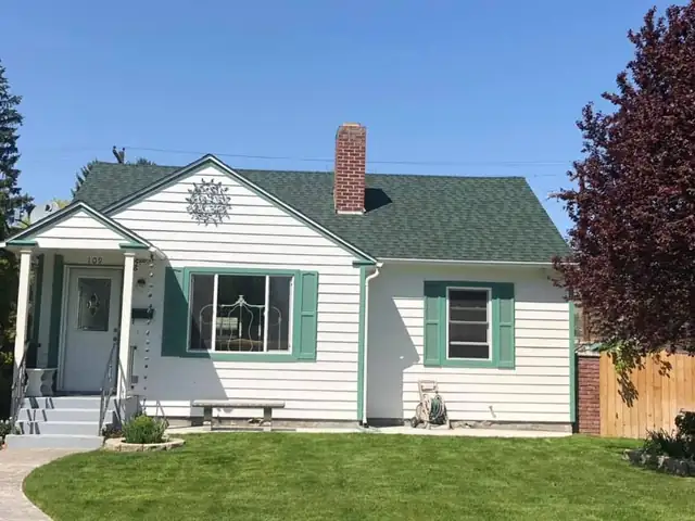 Single-story white lap-sided house with green trim and shutters, a covered entry and a green roof
